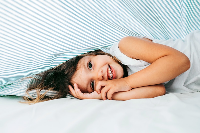 young girl smiling in bed under sheet